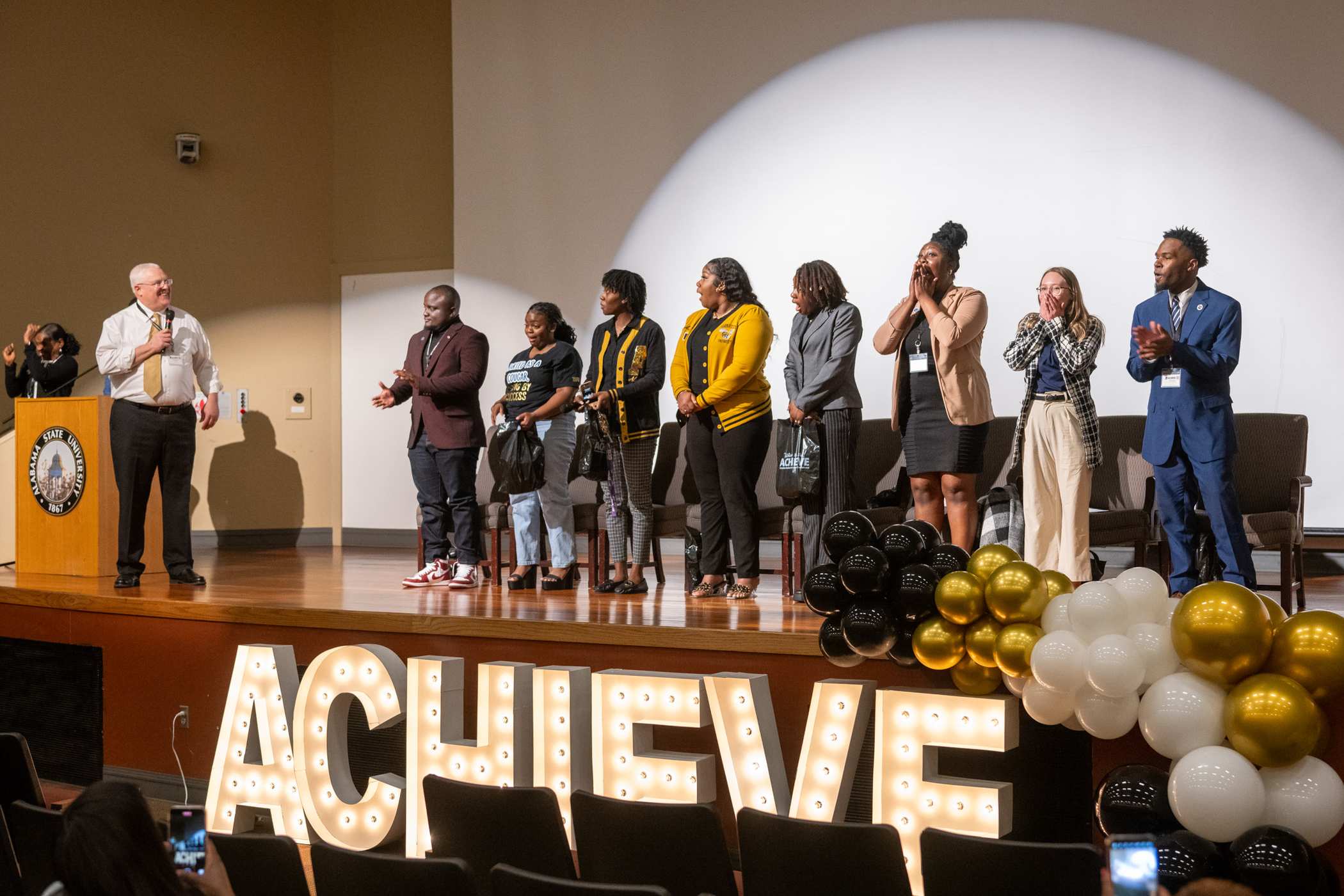 ASU Staff standing on a stage with a large sign below spelling 'ACHIEVE'